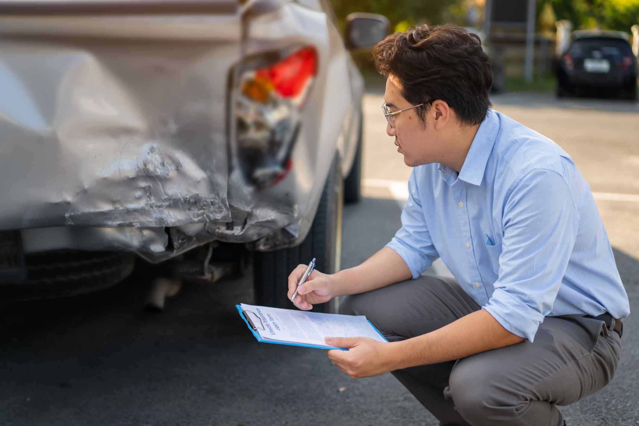 Man inspecting a damaged car and taking notes.